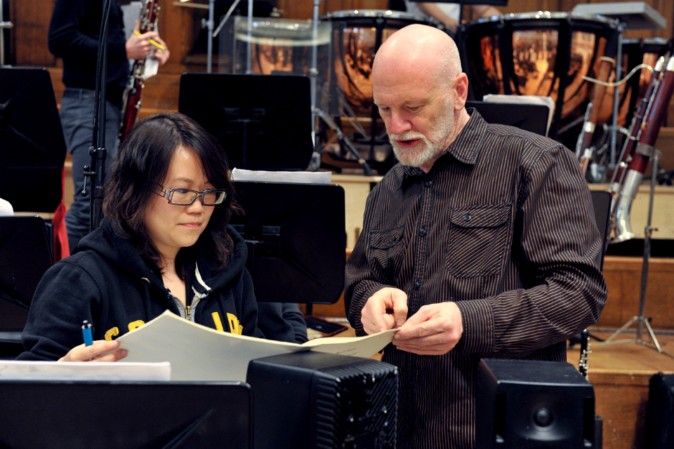 Brett Dean with a student looking at a musical score with orchestral instruments behind them